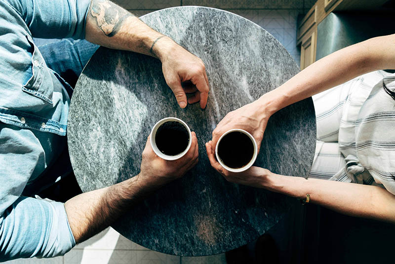 overhead view of two people holding coffee cups at small table