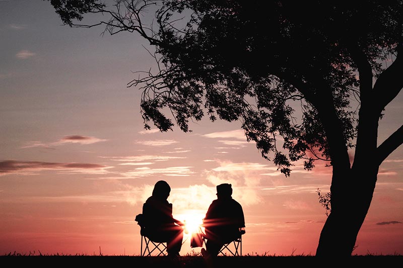 two people talk outside by a tree at dusk