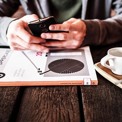 man texts on phone at table with book and coffee