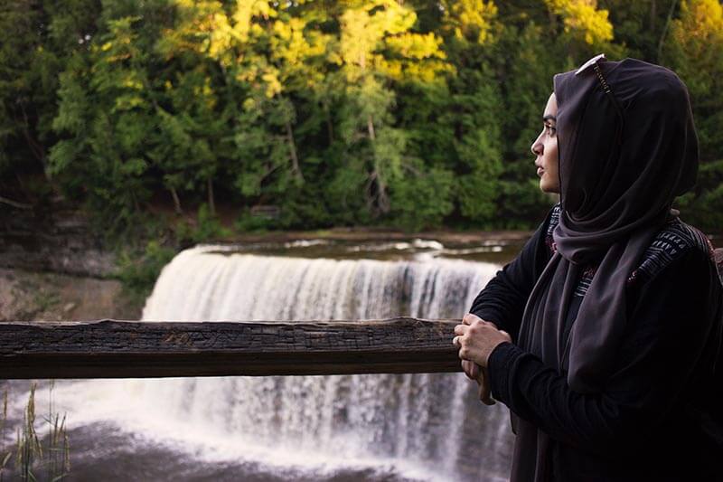 woman in hijab looks out at waterfall