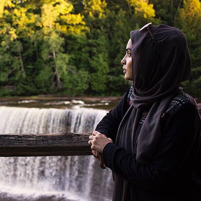 woman in hijab looks out at waterfall