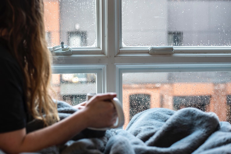 woman holding coffee in front of a rainy window